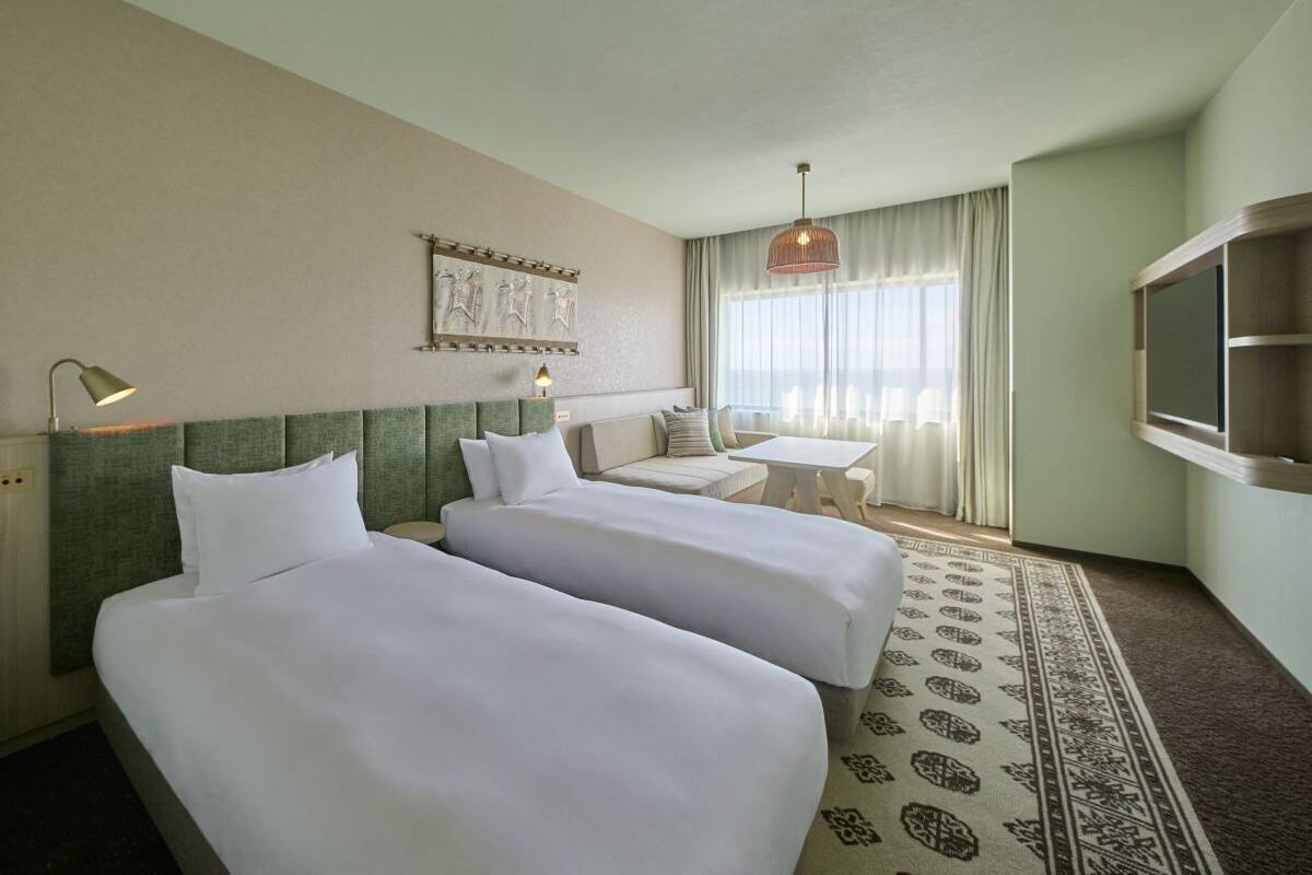 A hotel room with two beds, a sofa, a small table, a TV, and a patterned rug.