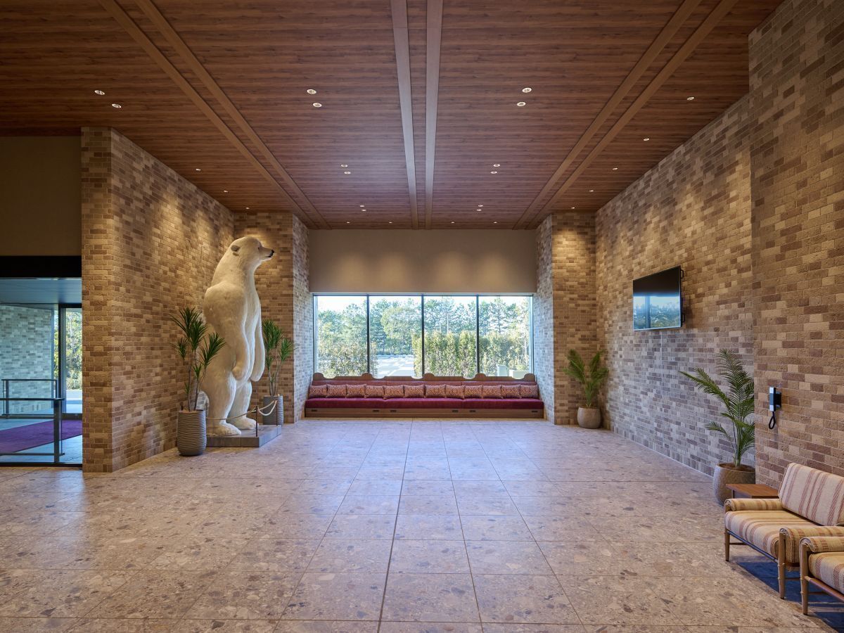 Un vestíbulo amplio con una gran escultura de oso de piedra, un banco rojo y un televisor montado en la pared de ladrillo.