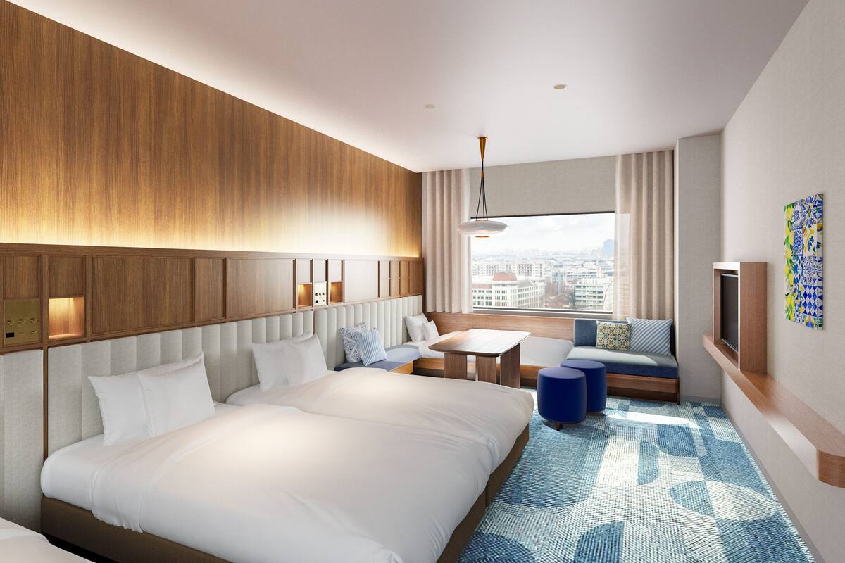 A modern hotel room with a large bed, a sofa, a small table, and a city view through the window.