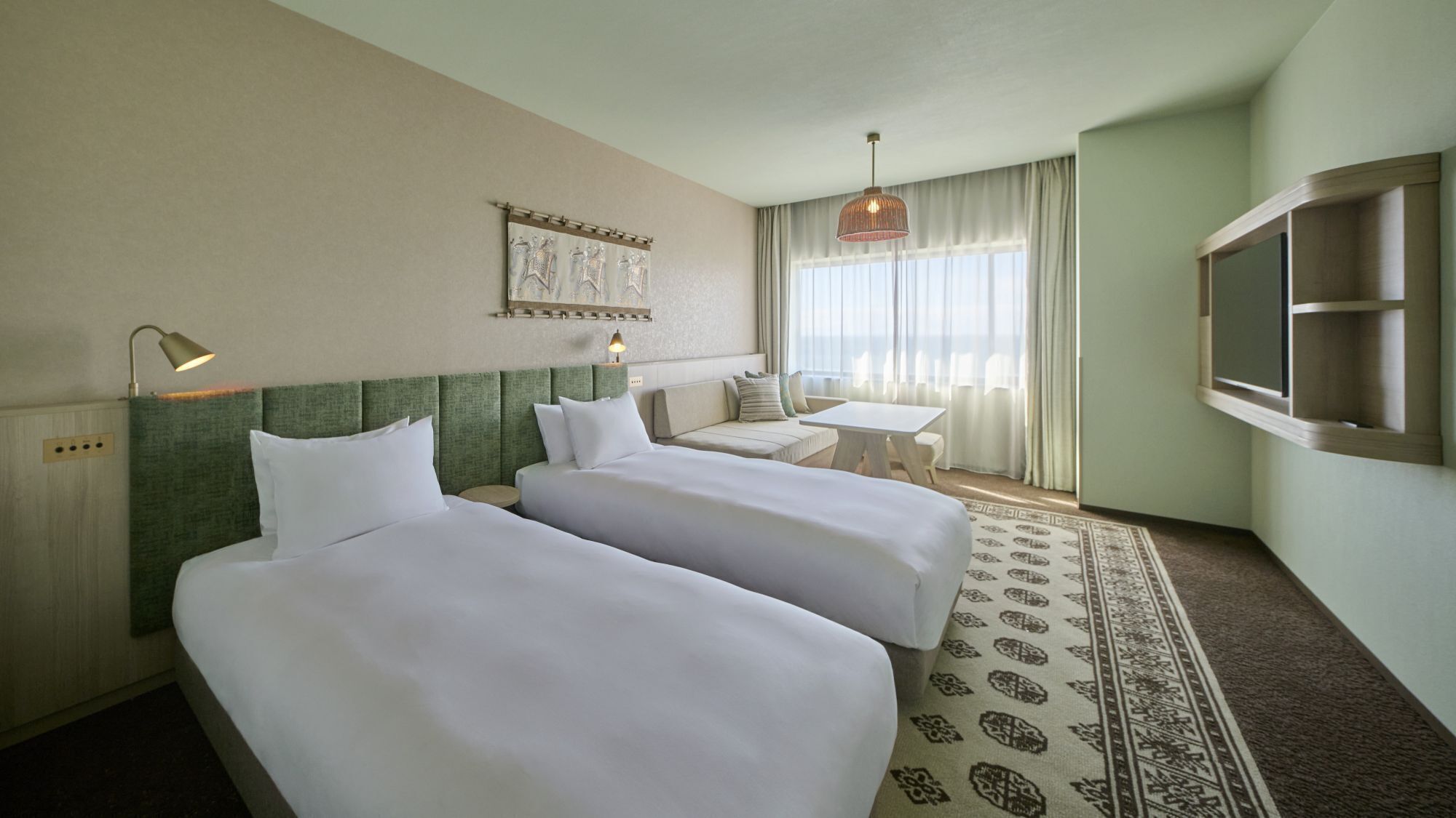 A hotel room with two beds, a small table, a TV, and a patterned rug.