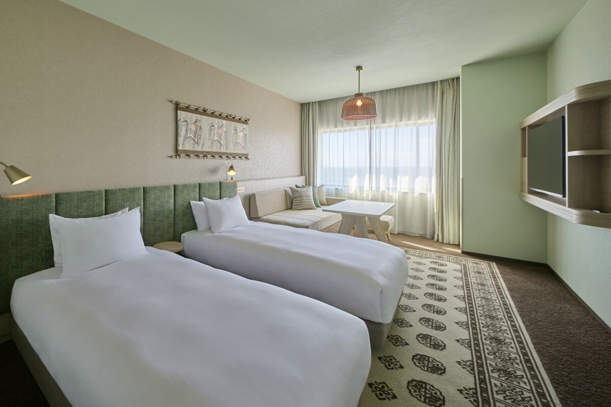 A hotel room with two beds, a small table, a TV, and a patterned rug.