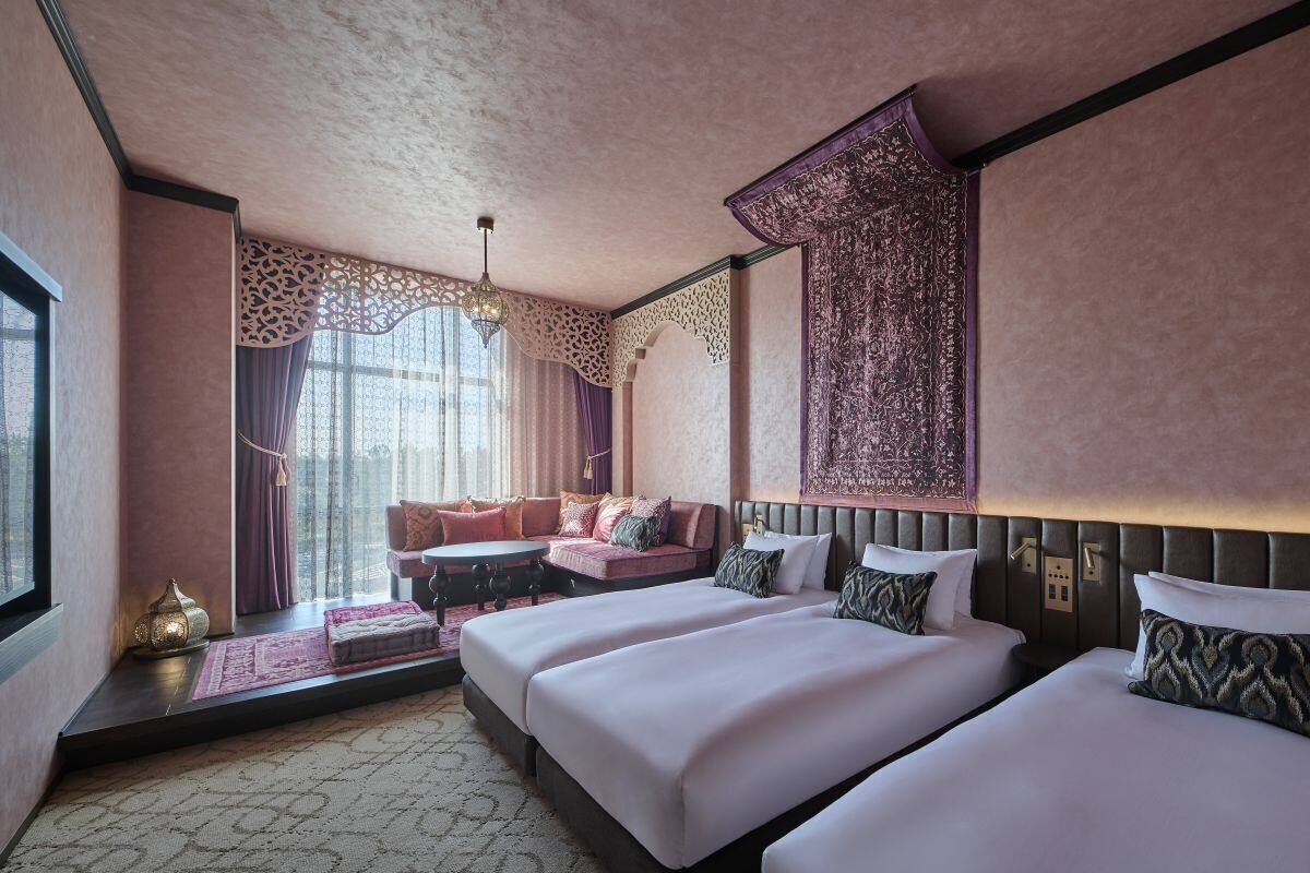 A hotel room with two beds, a sofa, a patterned rug, and a decorative wall hanging.