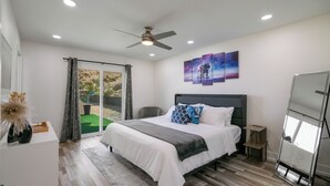 Un dormitorio con una cama, un ventilador de techo, vista a través de una puerta corrediza y una pared con tres cuadros.