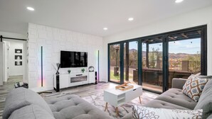 Una sala de estar moderna con un televisor de pantalla plana, un mueble blanco para equipo multimedia, un sofá y una puerta corrediza de vidrio que da a un patio exterior.