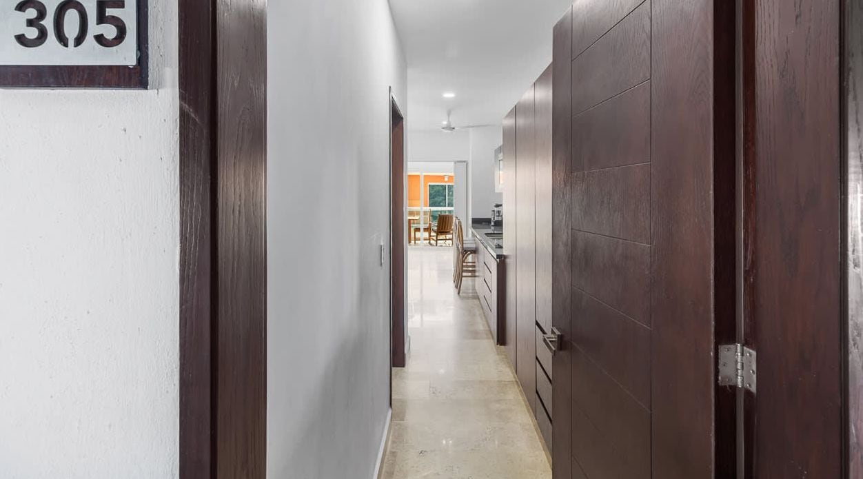 A hallway with a number sign, wooden doors, and a view into a room with a dining area.
