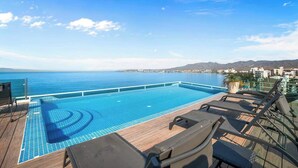 A swimming pool with a view of the sea, lounge chairs, and a wooden deck. - Risco 305: Downtown, Rooftop Pool, & Beach Access (Bucerías)