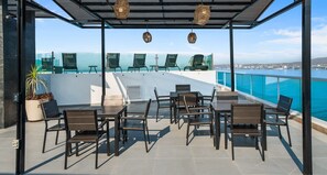 Terraza al aire libre con sillas y mesas, con vista a un cuerpo de agua.