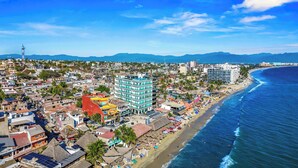 A coastal cityscape with a beach, buildings, and a clear sky. - Risco 305: Downtown, Rooftop Pool, & Beach Access (Bucerías)