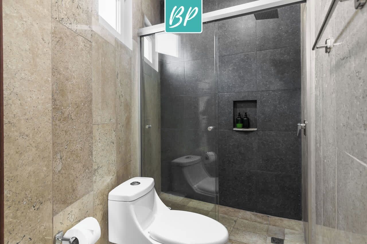 A modern bathroom with a toilet, a glass-enclosed shower stall, and a small shelf with toiletries.