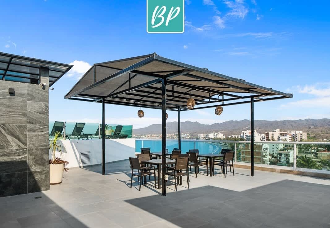 Terraza en la azotea con zona de estar cubierta, piscina y vistas a la ciudad y las montañas.