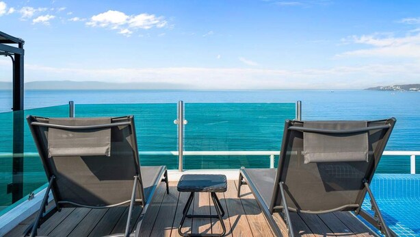 A deck with two chairs and a small table, overlooking a clear blue sea and distant land. - Risco 305: Downtown, Rooftop Pool, & Beach Access (Bucerías)
