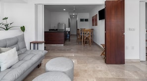 Uma sala de estar moderna com sofá, banquinho e área de jantar com cadeiras e mesa.