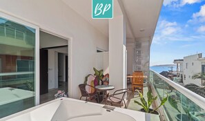 Ein Balkon mit Glasgeländer, einem kleinen Tisch mit Stühlen und Topfpflanzen.