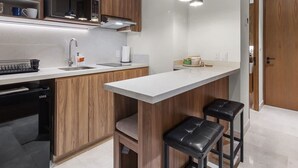 A modern kitchen with wooden cabinets, a white countertop, a built-in oven, and two black bar stools.