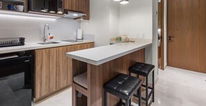 A modern kitchen with wooden cabinets, a white countertop, a built-in oven, and two black bar stools.