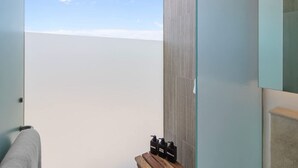 A bathroom with a large window, a wooden bench, and toiletries on the bench.
