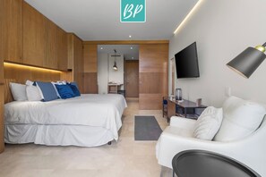 A modern hotel room with a large bed, a desk, a TV, and a sofa.