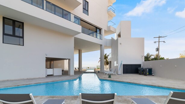 A modern building with a swimming pool, outdoor seating, and a view of the ocean.