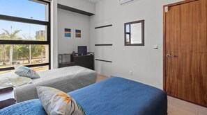 A bedroom with a bed, a desk, a chair, a wardrobe, and a window with a view of trees and buildings. - 2BR, Rooftop Pool w/ Views, & Parking: Vista 101 (Bucerías)