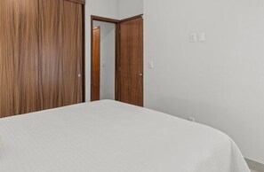 A bedroom with a bed, wooden wardrobe, and a door leading to another room. - 2BR, Rooftop Pool w/ Views, & Parking: Vista 101 (Bucerías)