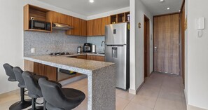 A modern kitchen with granite countertops, wooden cabinets, a stainless steel refrigerator, and a built-in microwave. - 2BR, Rooftop Pool w/ Views, & Parking: Vista 101 (Bucerías)
