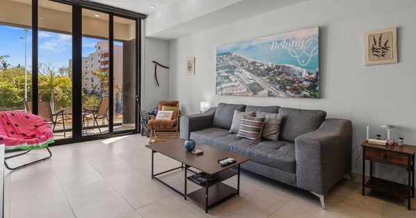 A modern living room with a grey sofa, a coffee table, and a cityscape painting on the wall. - 2BR, Rooftop Pool w/ Views, & Parking: Vista 101 (Bucerías)