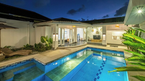 A swimming pool with a tiled deck, a covered outdoor seating area, and a well-lit interior space. - LaLeBay Seminyak (Seminyak)