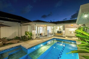 A swimming pool with a tiled deck, a covered outdoor seating area, and a well-lit interior space. - LaLeBay Seminyak (Seminyak)