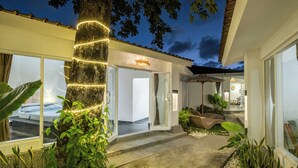 A modern house with a well-lit entrance, a visible staircase, and a patio area with plants and a seating arrangement. - LaLeBay Seminyak (Seminyak)