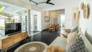 A spacious living area with a TV, wooden furniture, and a ceiling fan. - LaLeBay Seminyak (Seminyak)