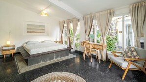 A modern bedroom with a large bed, a desk, and a chair, featuring a view of greenery outside. - LaLeBay Seminyak (Seminyak)