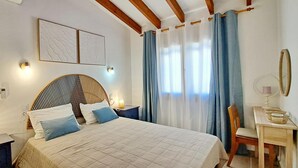 Un dormitorio con cama, lámparas de noche, un escritorio con silla, un espejo y cortinas.