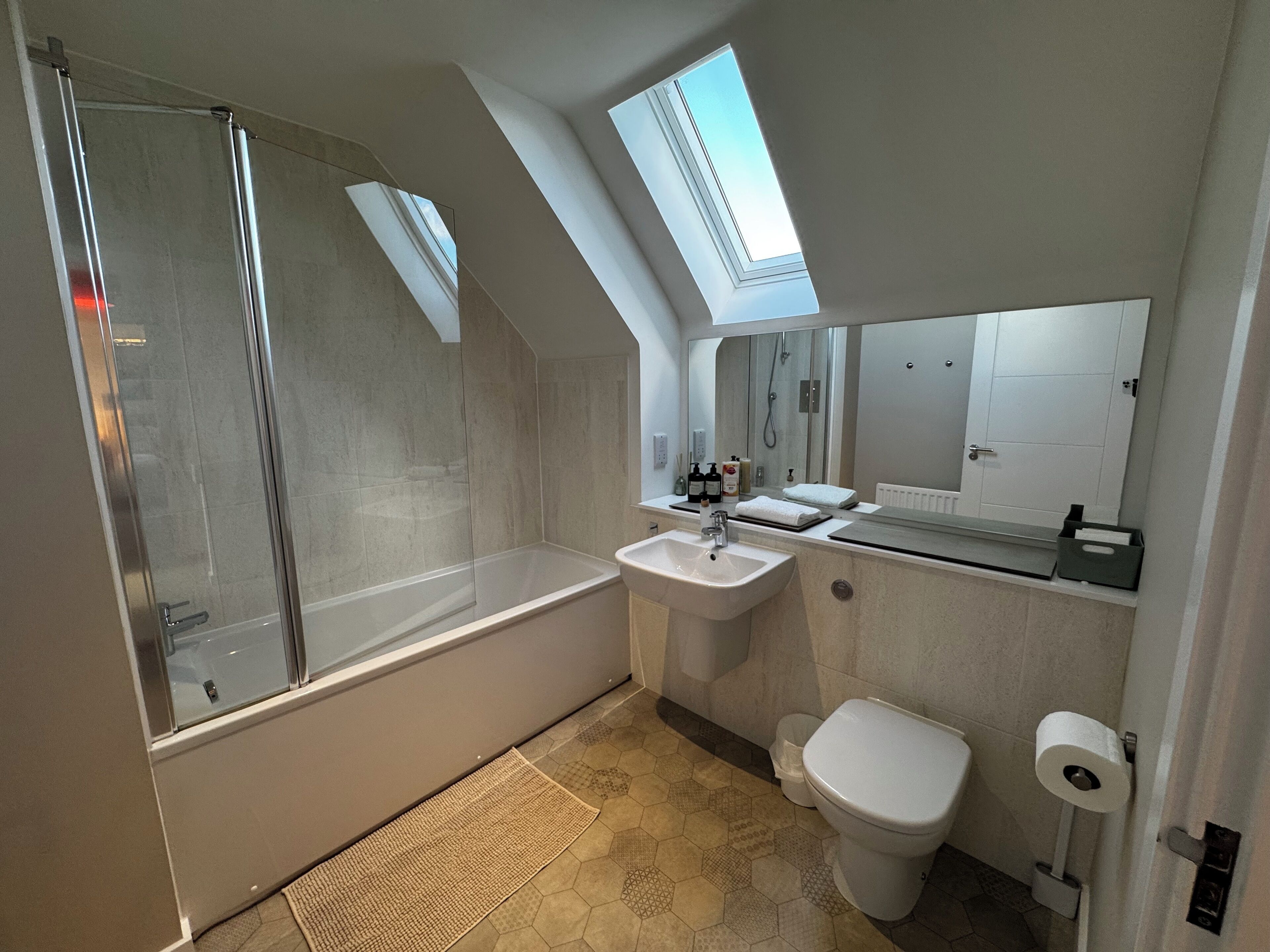 Un bagno moderno con doccia vetrata, lavandino, WC e finestra a lucernario.