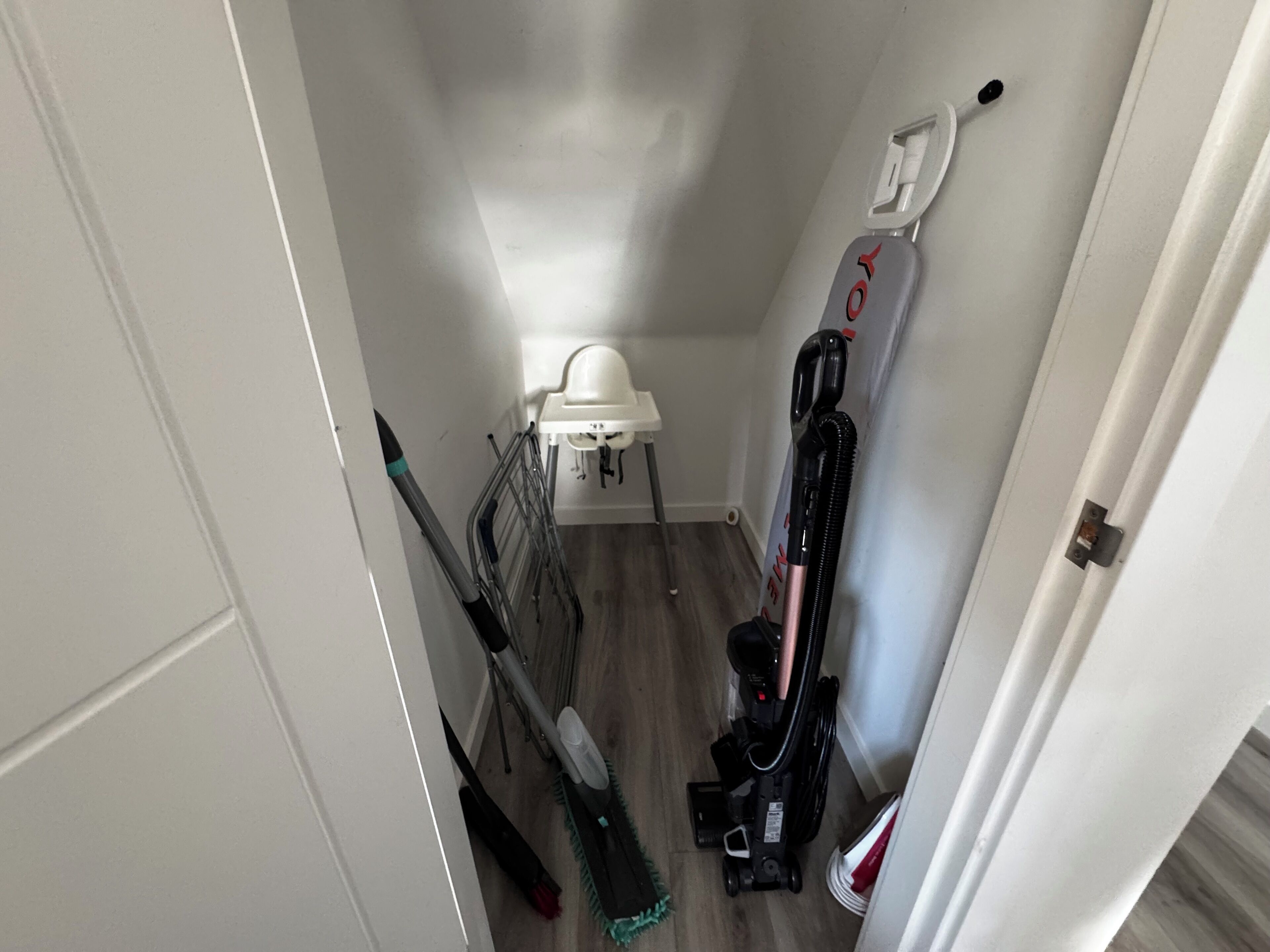Ein schmaler Flur mit Staubsauger, Besen und Kehrschaufel, die an der Wand lehnen.