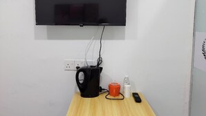 A small room with a wooden table, a black kettle, a red mug, a remote control, and a blue laundry basket. - The Ardens Hotel - Pekan Nenas (Pekan Nanas)