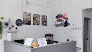 A reception area with a grey reception desk, a clock, framed floral artwork, and a wall-mounted poster. - The Ardens Hotel - Pekan Nenas (Pekan Nanas)