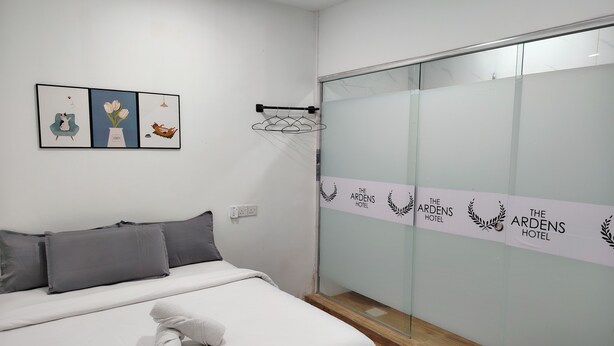 A hotel room with a bed, a small table, a wall-mounted TV, and a sliding door with the hotel's name. - The Ardens Hotel - Pekan Nenas (Pekan Nanas)