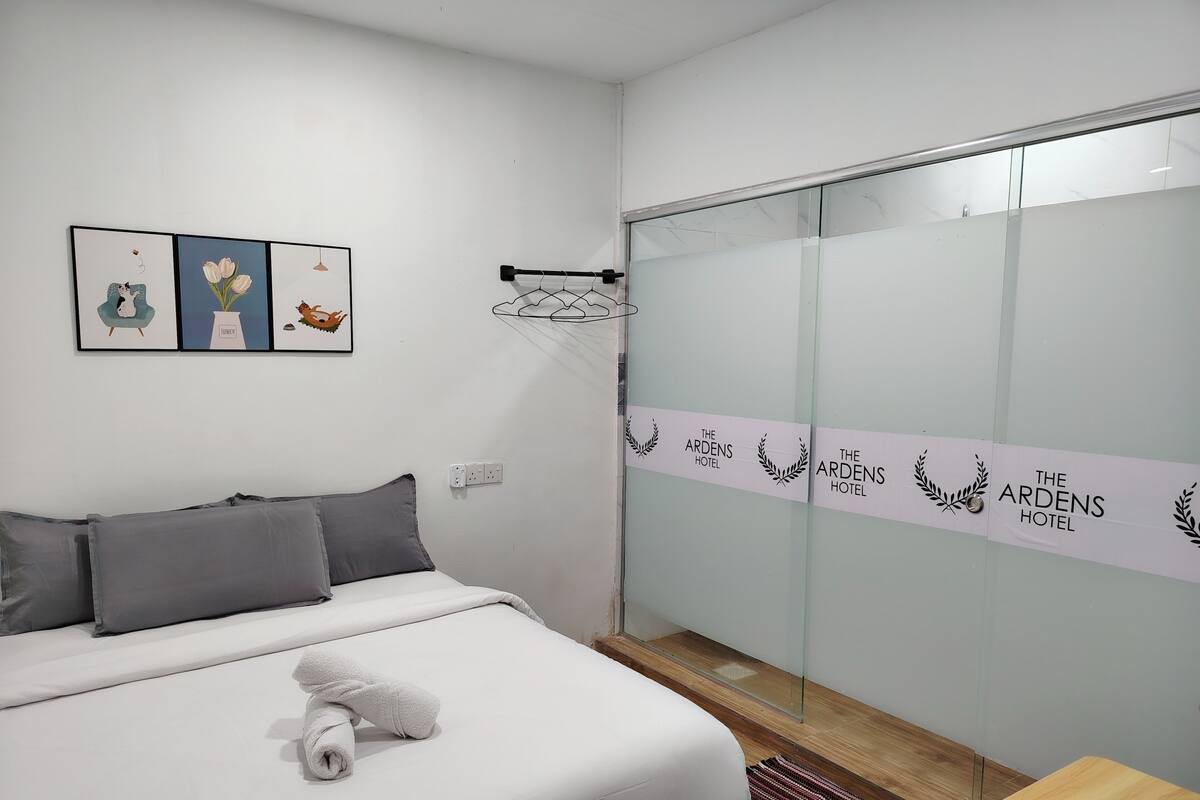 A hotel room with a bed, a small table, a wall-mounted TV, and a sliding door with the hotel's name.