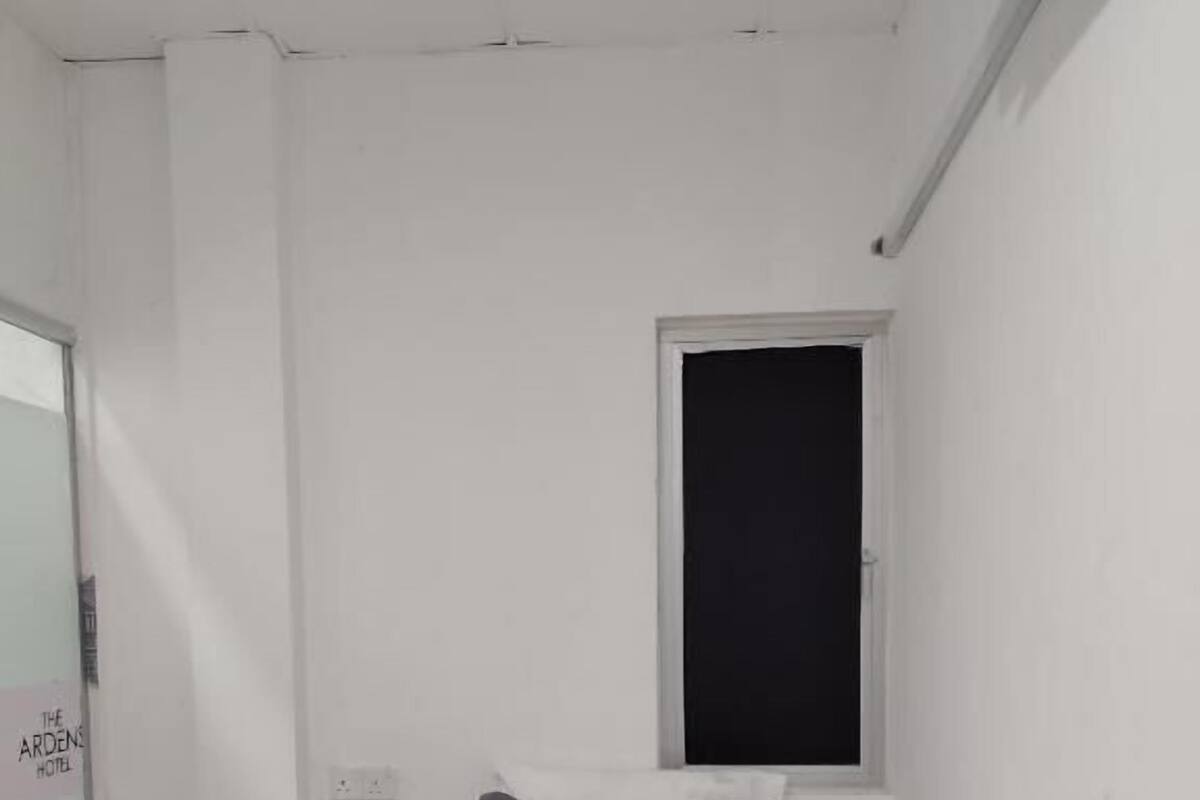 A small, single-bed room with a window, a pillow, and a rolled towel on the bed.