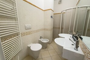 A bathroom with a toilet, bidet, and sink, featuring tiled walls and a mirror.