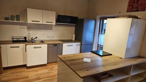 Een kleine keuken met witte kastjes, een ingebouwde magnetron, een koelkast en een houten aanrecht.