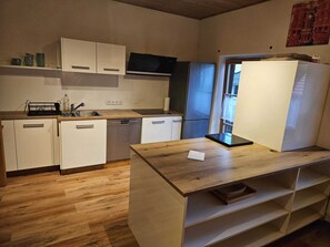 A compact kitchen with white cabinets, a built-in microwave, a refrigerator, and a wooden countertop.
