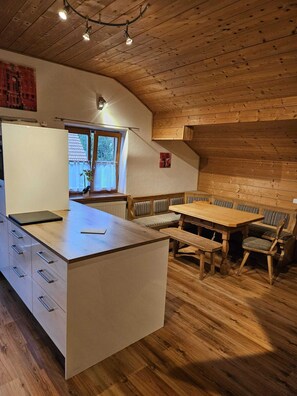 A cozy kitchen with a wooden ceiling, a dining area with a bench, and a window with a view.
