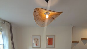 Un salon moderne avec un canapé d’angle gris, une table basse blanche et un luminaire suspendu original en fibres tressées. Deux œuvres d’art encadrées sont exposées au mur.