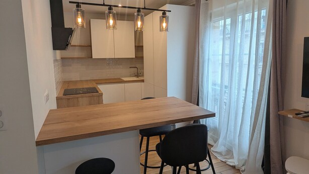 Une cuisine moderne avec un plan de travail en bois, des tabourets de bar noirs et des luminaires suspendus.