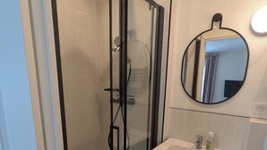 Une salle de bain moderne avec une douche à parois de verre, un lavabo blanc avec un miroir au-dessus et un meuble gris en dessous.