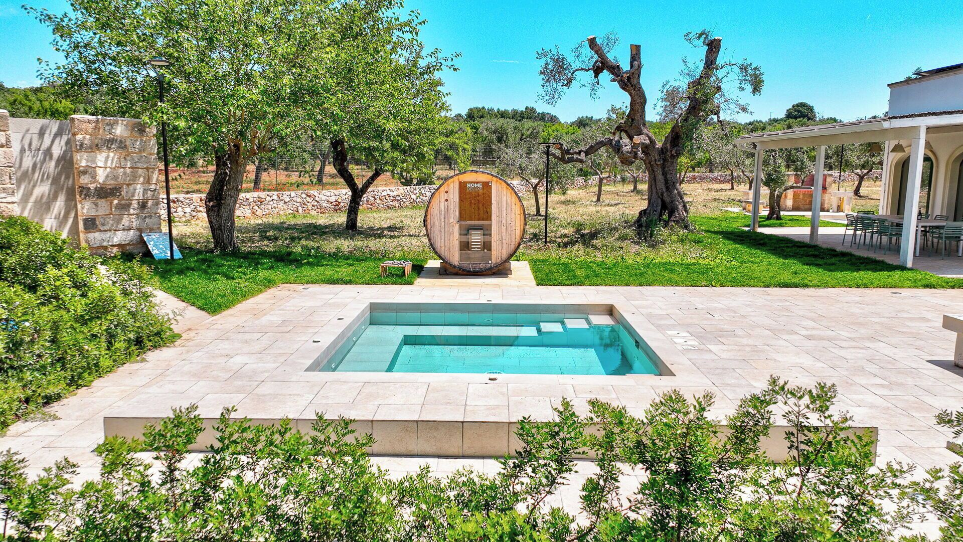 Una piscina con una estructura de barril de madera en el centro, rodeada por un muro de piedra y vegetación.