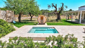 Una piscina amb una estructura de bótes de fusta al centre, envoltada per una paret de pedra i vegetació.