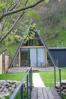 Una cabaña moderna tipo A con fachada de vidrio, terraza de madera y pared de piedra frontal.
