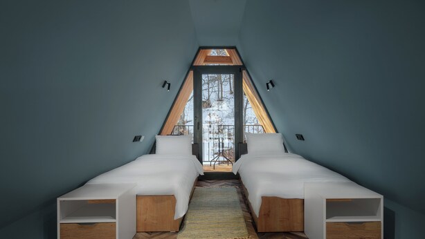A bedroom with two beds, a herringbone-patterned wooden floor, and a view of a snowy landscape through a triangular window. - Ari Home Aghveran (Agveran)